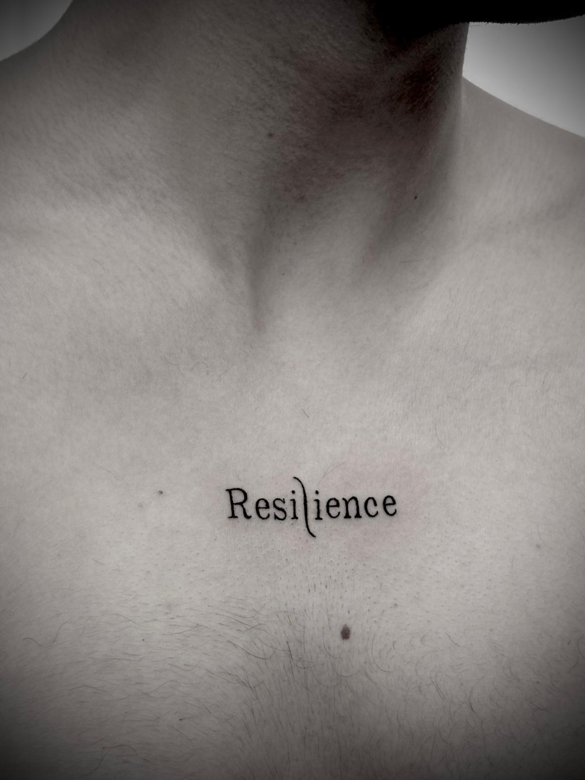 Tatuagem lettering 'Resilience' no peito por Heltattoo